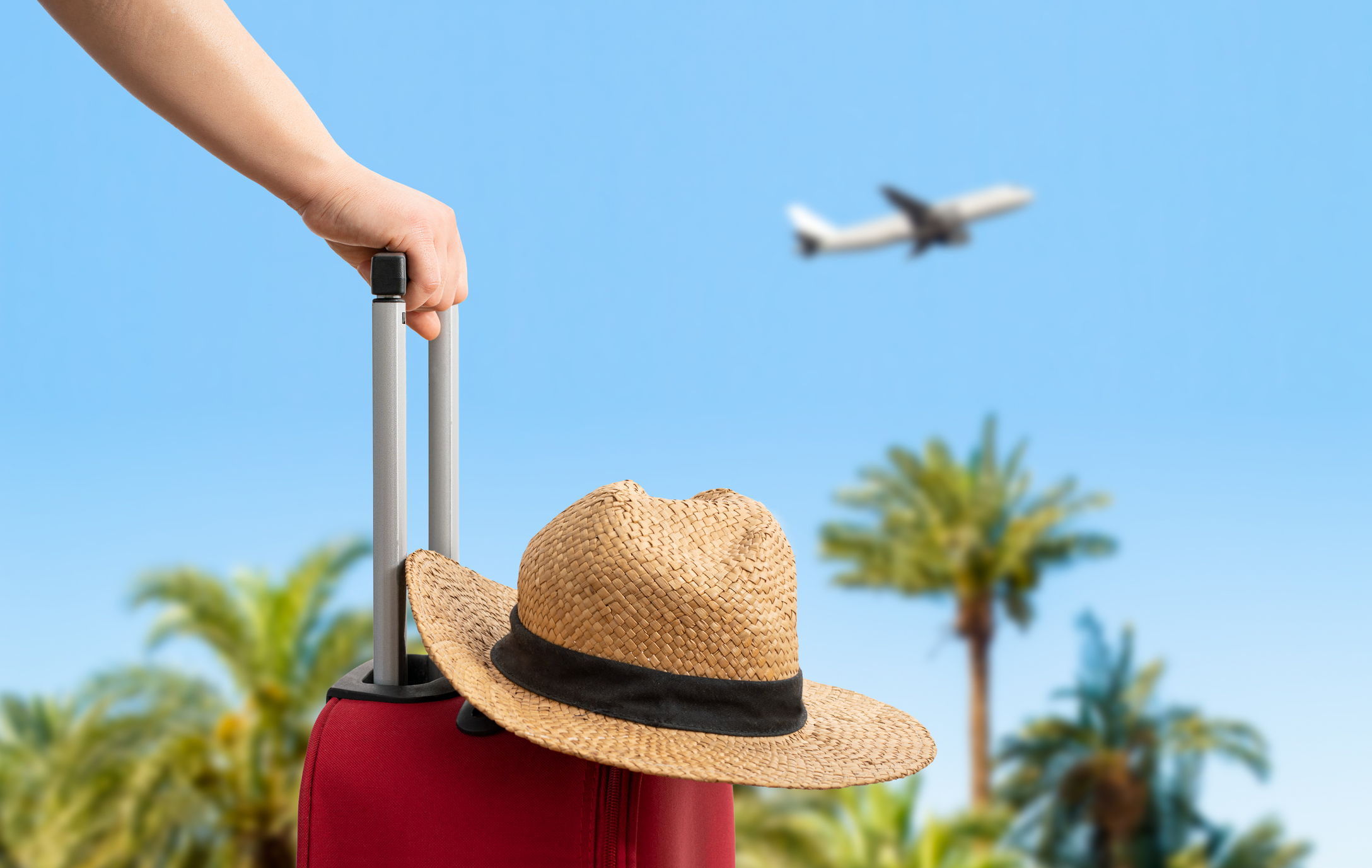 Suitcase with a sun hat and an airplane in the background