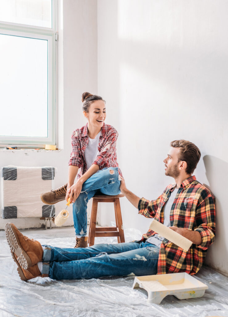 Smiling young couple holding paint rollers and talking in new apartment