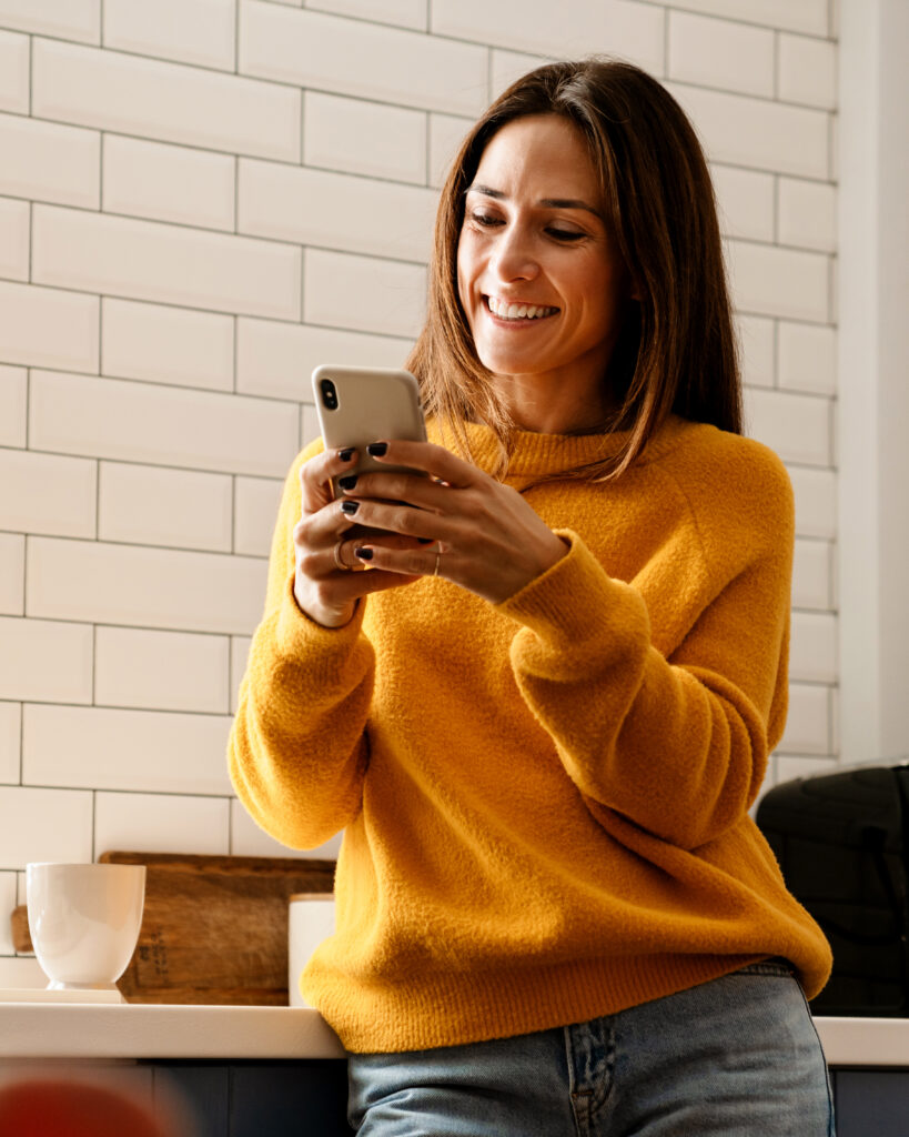 Woman smiling at mobile phone in kitchen